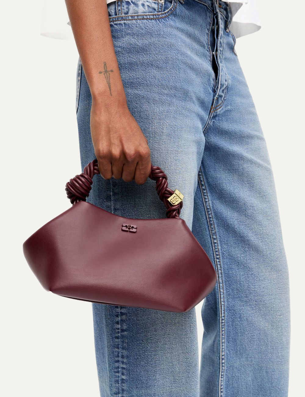 Model holding small burgundy Ganni Bou Bag with twisted handle