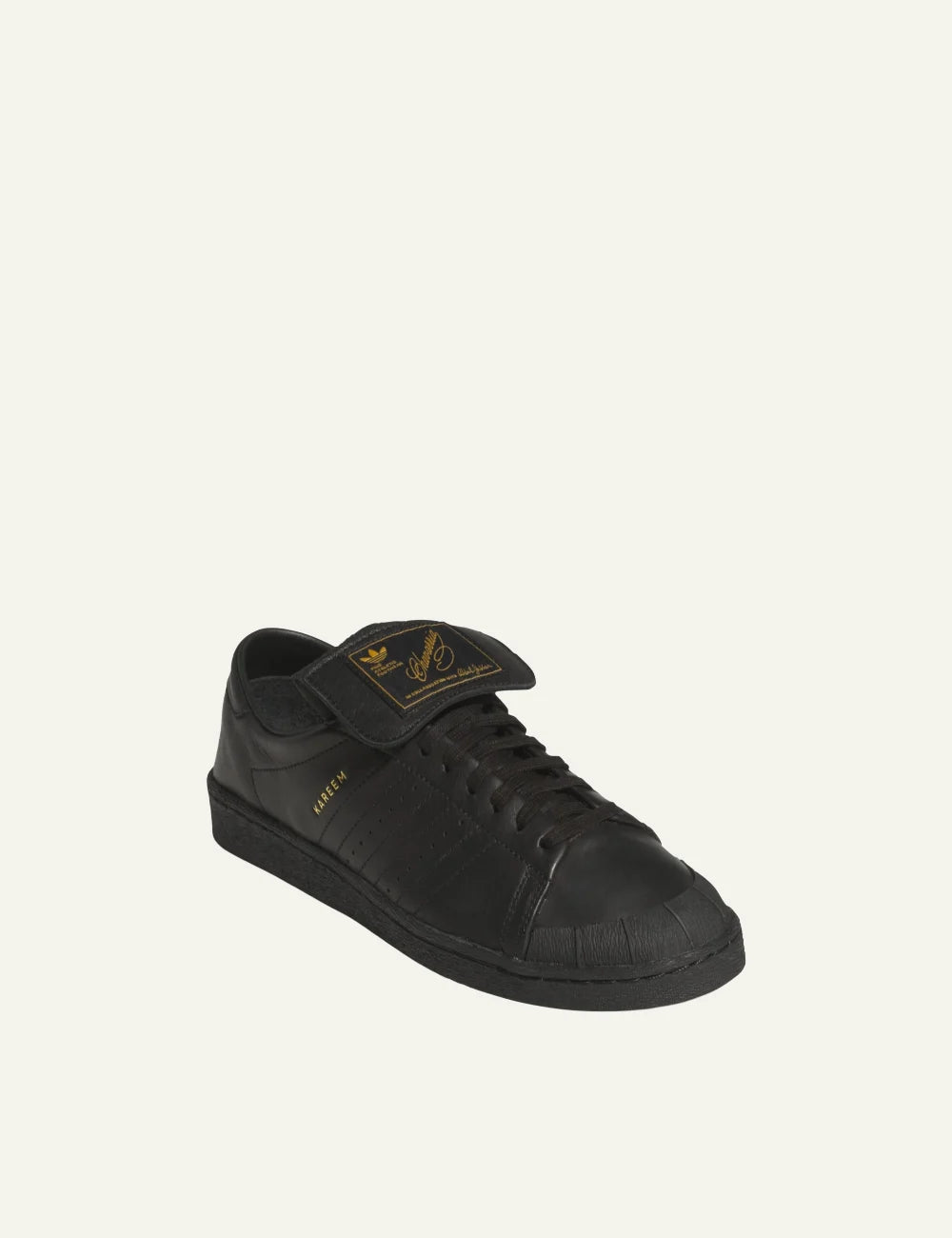 Angled view: Premium black leather Jabbar low-top sneaker with gold Kareem branding και oversized tongue detail.