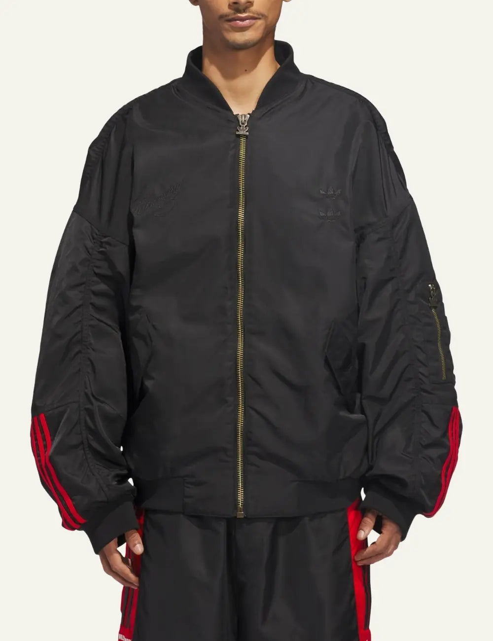 Model wearing Adidas x Willy Chavarria black satin bomber σε relaxed fit streetwear look.