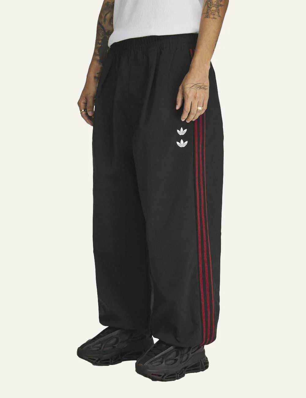 Men's adidas black woven track pants with burgundy side stripes, embroidered logos and rose artwork model