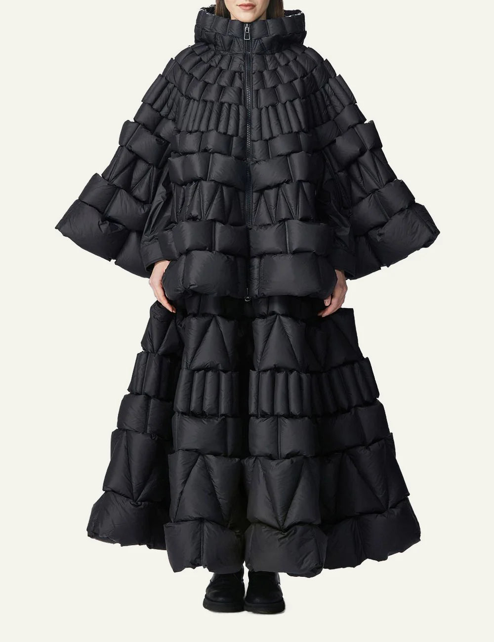 Raxxy black 3D quilted cape puffer σε front view on model, με sculptural padded blocks και dramatic full-length silhouette.