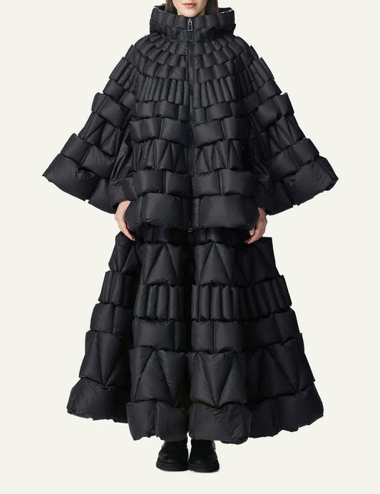 Raxxy black 3D quilted cape puffer σε front view on model, με sculptural padded blocks και dramatic full-length silhouette.