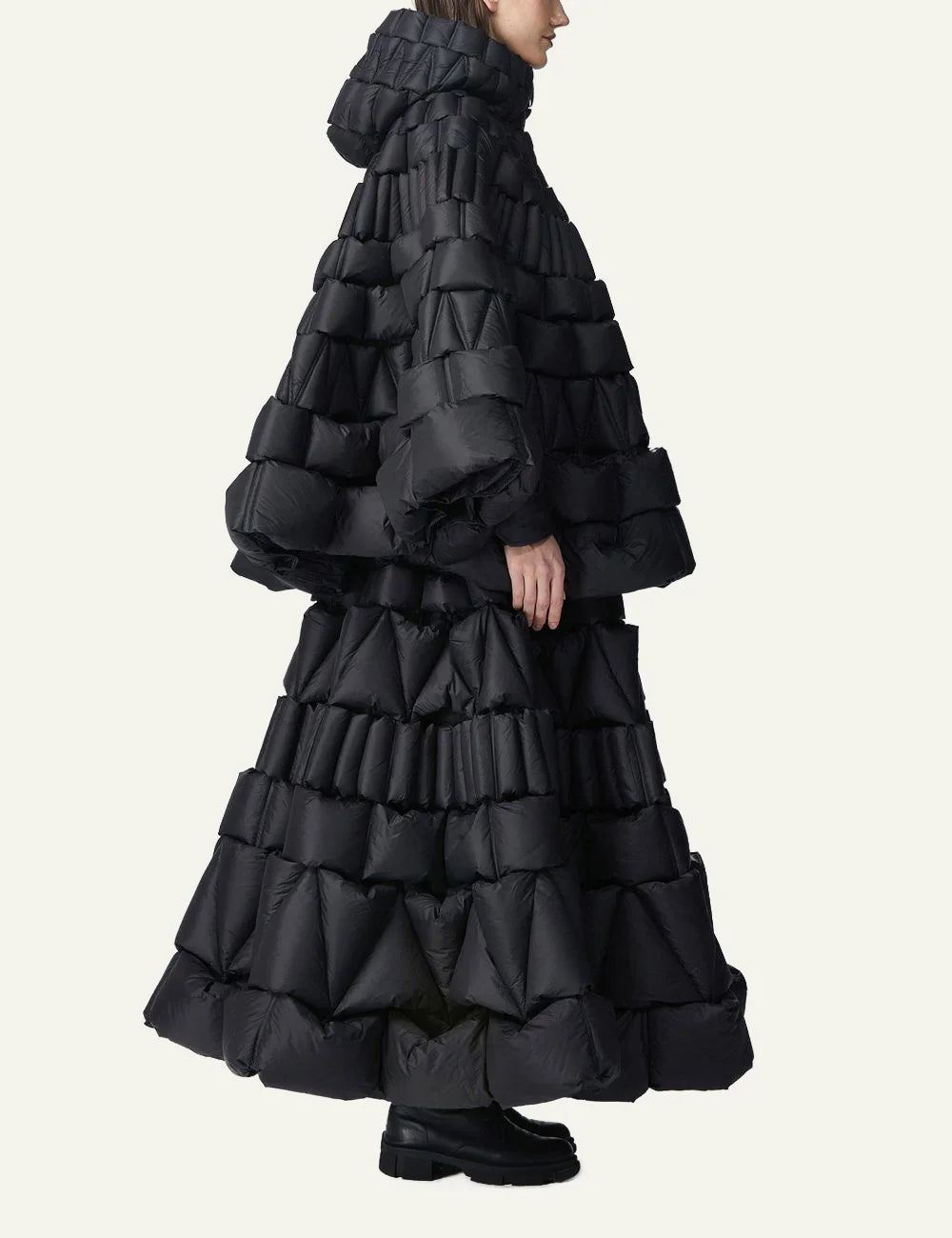 Side view of Raxxy black 3D quilted cape puffer, με geometric layered padding και oversized avant-garde shape.