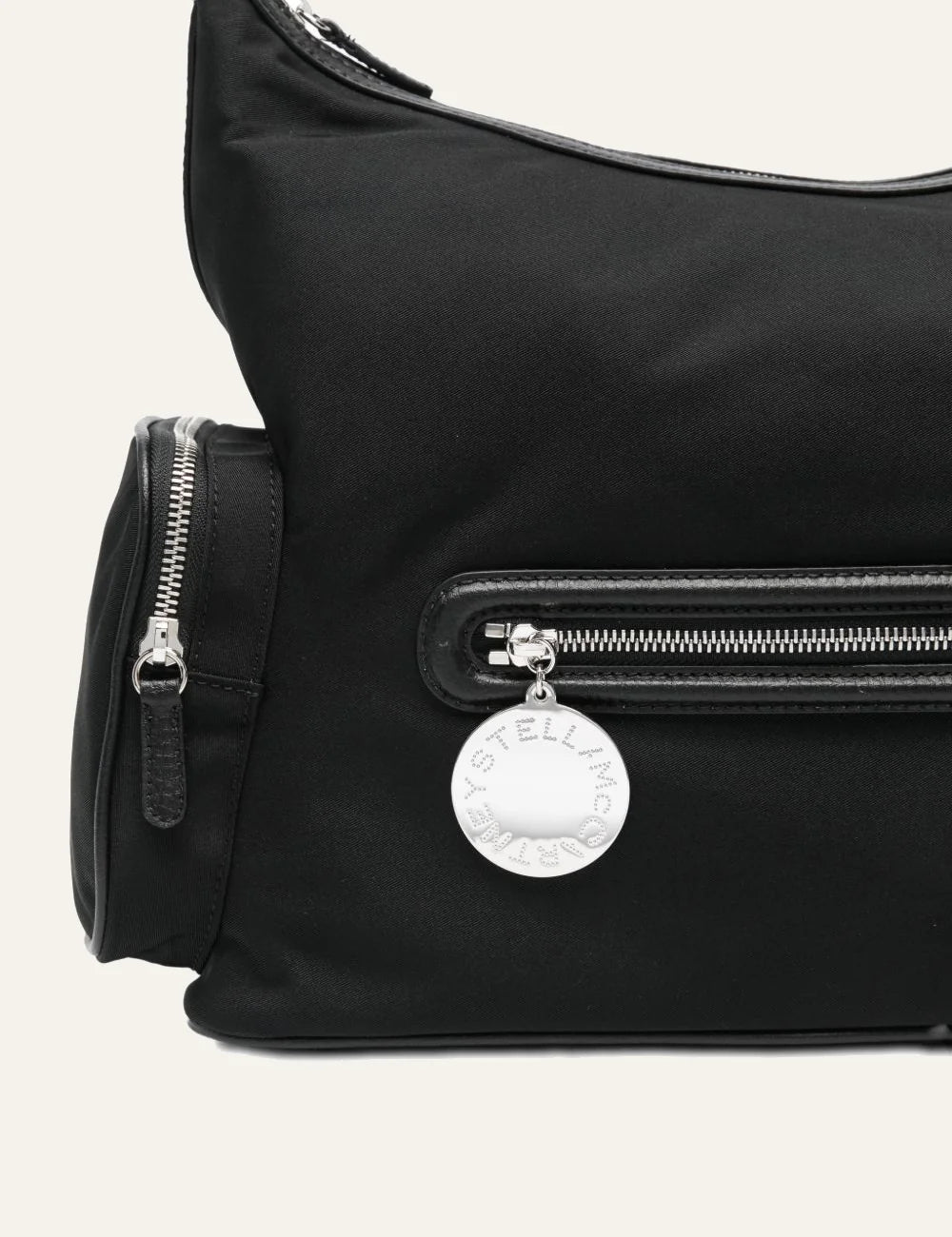 “Close-up of Stella McCartney black Dartmoor bag με silver zip και engraved circular logo charm.”