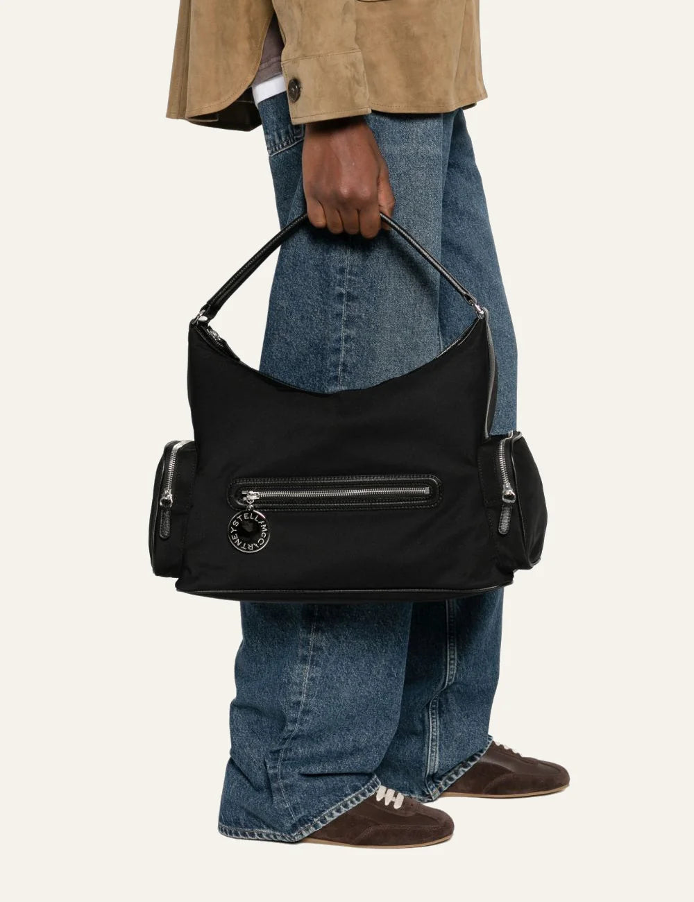 “Model holding the Stella McCartney Dartmoor black shoulder bag with utilitarian side pockets and logo charm.”