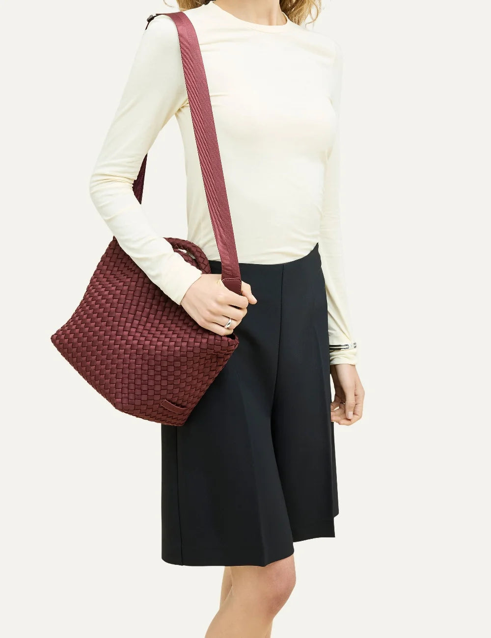 Women's Naghedi St. Barths Small Tote in Bordeaux handwoven neoprene with top handles and adjustable crossbody strap on model