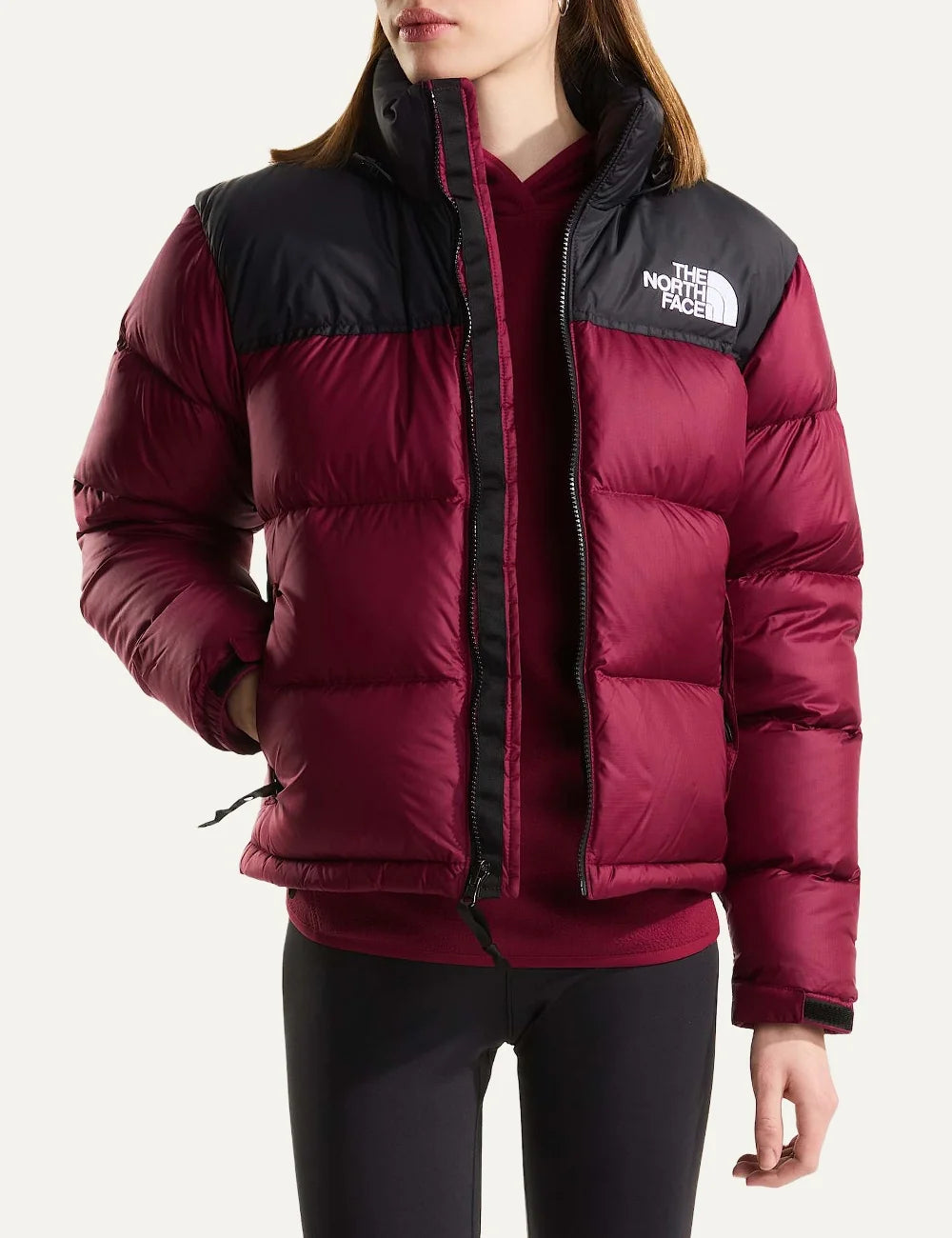 The North Face women's 1996 Retro Nuptse puffer jacket in burgundy and black with quilted down panels, high collar, front zipper and white chest logo model