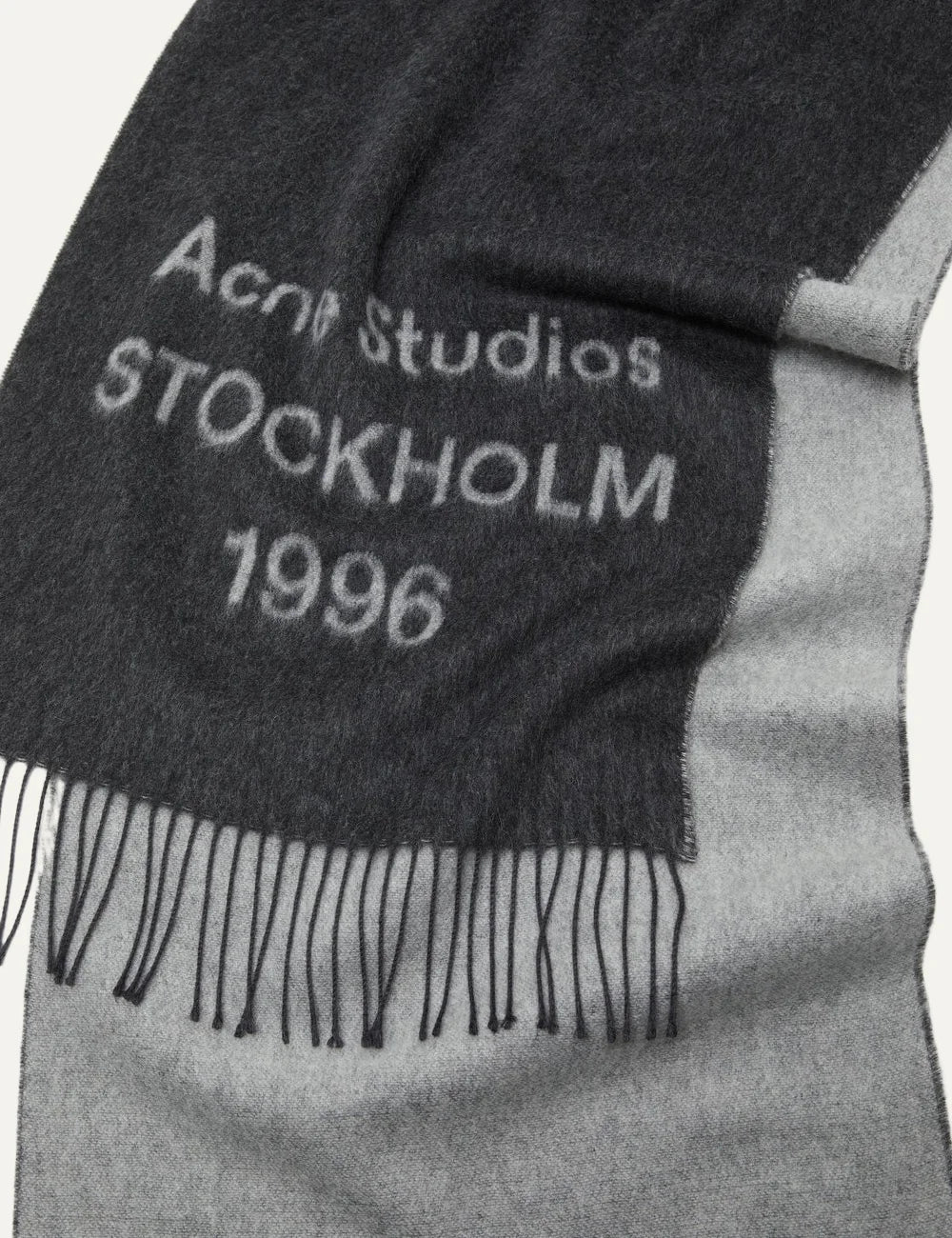 Acne Studios men's dark charcoal grey wool jacquard scarf featuring contrasting Acne Studios Stockholm 1996 logo lettering and fringed ends detail