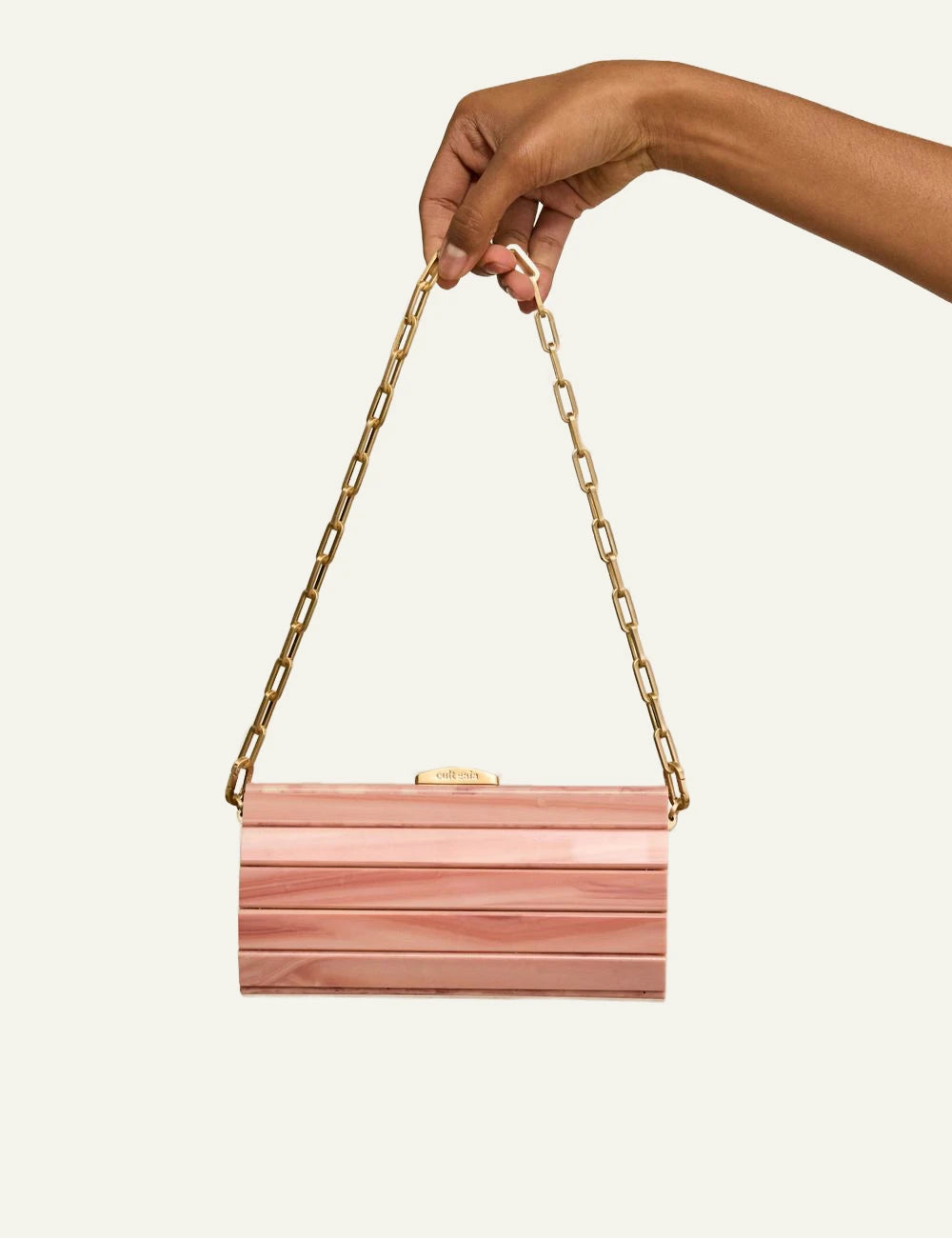 Cult Gaia pink acrylic clutch held by hand gold chain detail