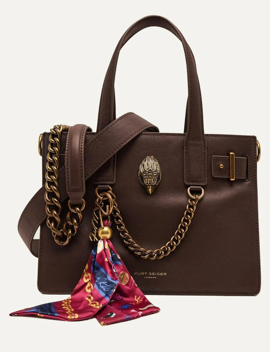 Kurt Geiger women's Sloane Small Tote dark brown leather handbag featuring structured rectangular silhouette, double top handles, leather shoulder strap, gold-tone chain detail, signature eagle head emblem and colorful burgundy printed scarf charm.