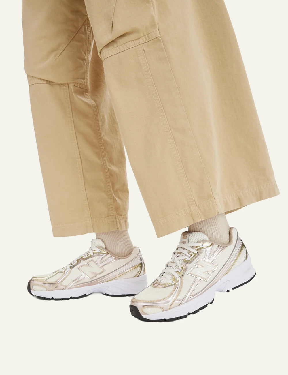 New Balance 740 women's beige sneakers with pink and gold metallic details worn by model