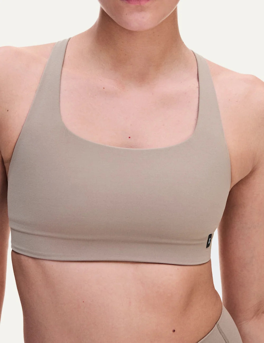 On women's beige sports bra with low support, scoop neckline, strappy open back, soft SenseTec stretch fabric, gentle elastic underband and moisture-wicking mesh lining.