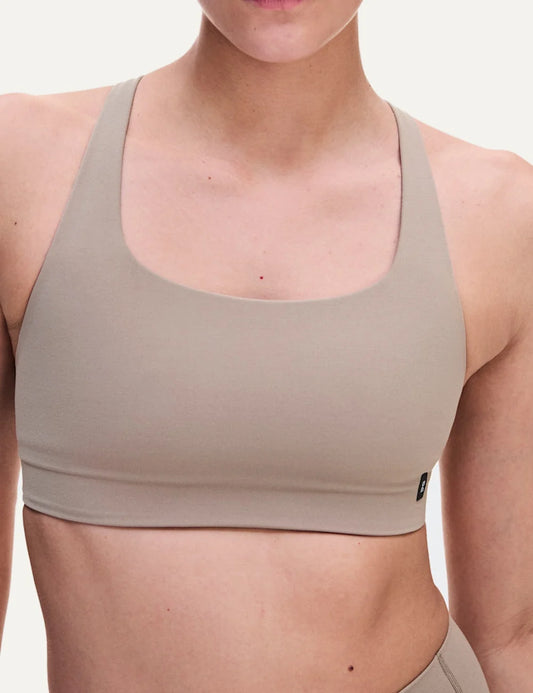 On women's beige sports bra with low support, scoop neckline, strappy open back, soft SenseTec stretch fabric, gentle elastic underband and moisture-wicking mesh lining.