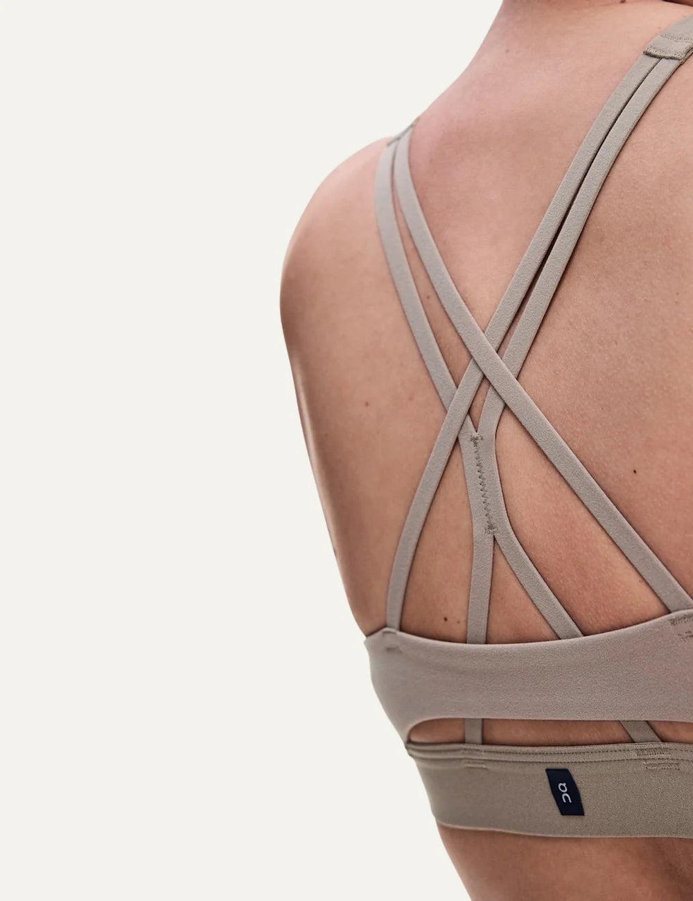 On women's beige sports bra with low support, scoop neckline, strappy open back, soft SenseTec stretch fabric, gentle elastic underband and moisture-wicking mesh lining detail