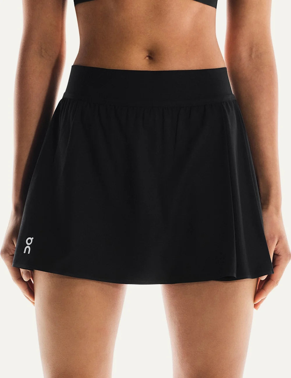 On women's black mini tennis skirt with subtle pleats, elastic waistband, integrated inner shorts, two pockets and On logo on the front.