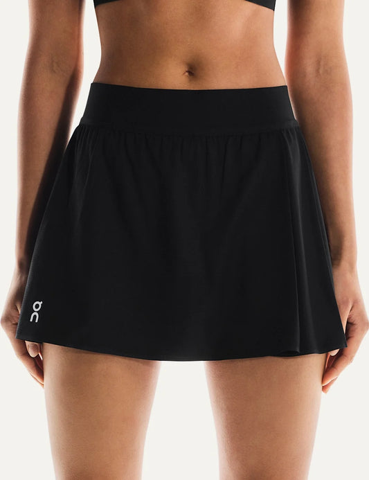 On women's black mini tennis skirt with subtle pleats, elastic waistband, integrated inner shorts, two pockets and On logo on the front.
