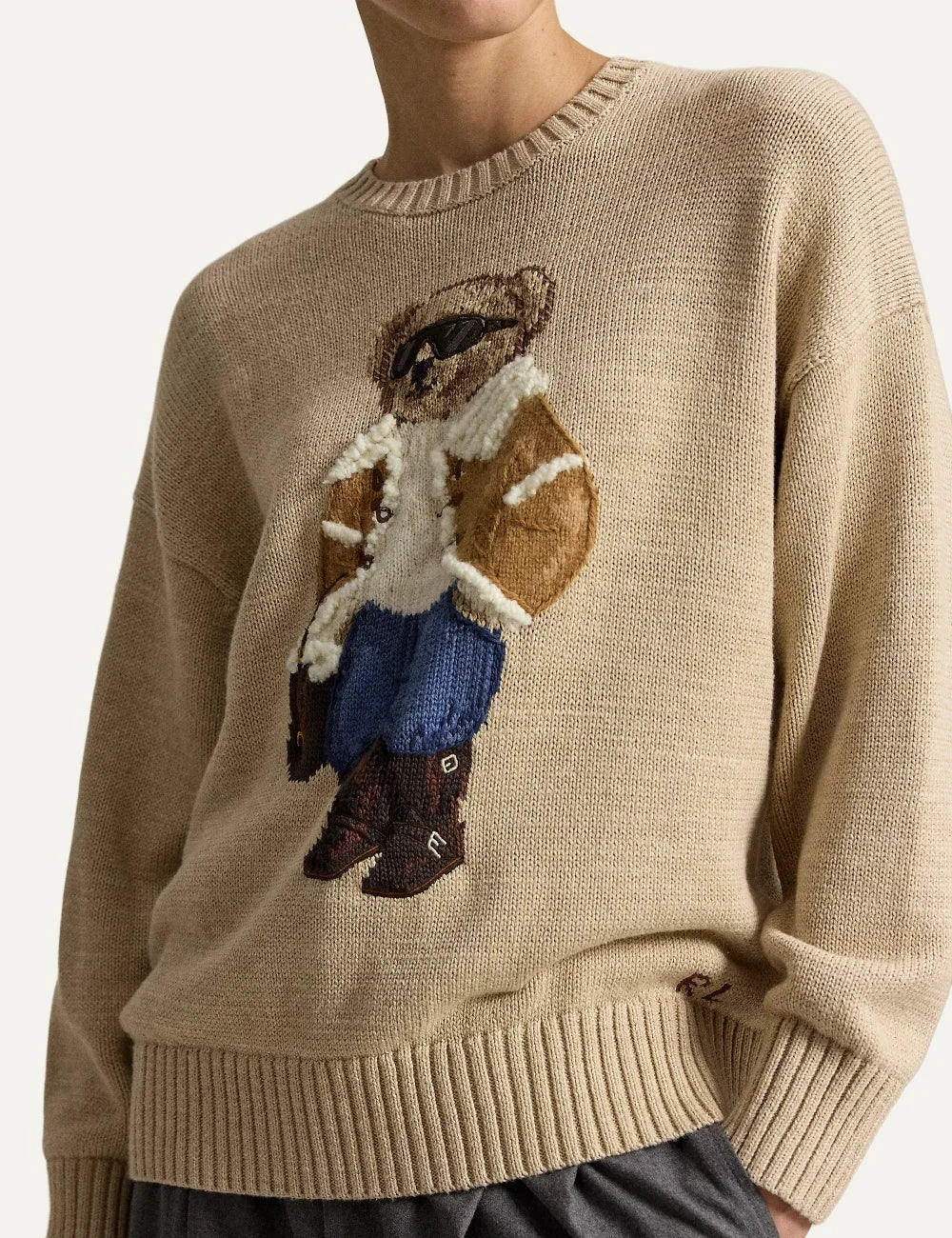 Polo Ralph Lauren men's beige cotton knit sweater featuring a Polo Bear in a shearling jacket, sunglasses and blue jeans, with ribbed trims full model
