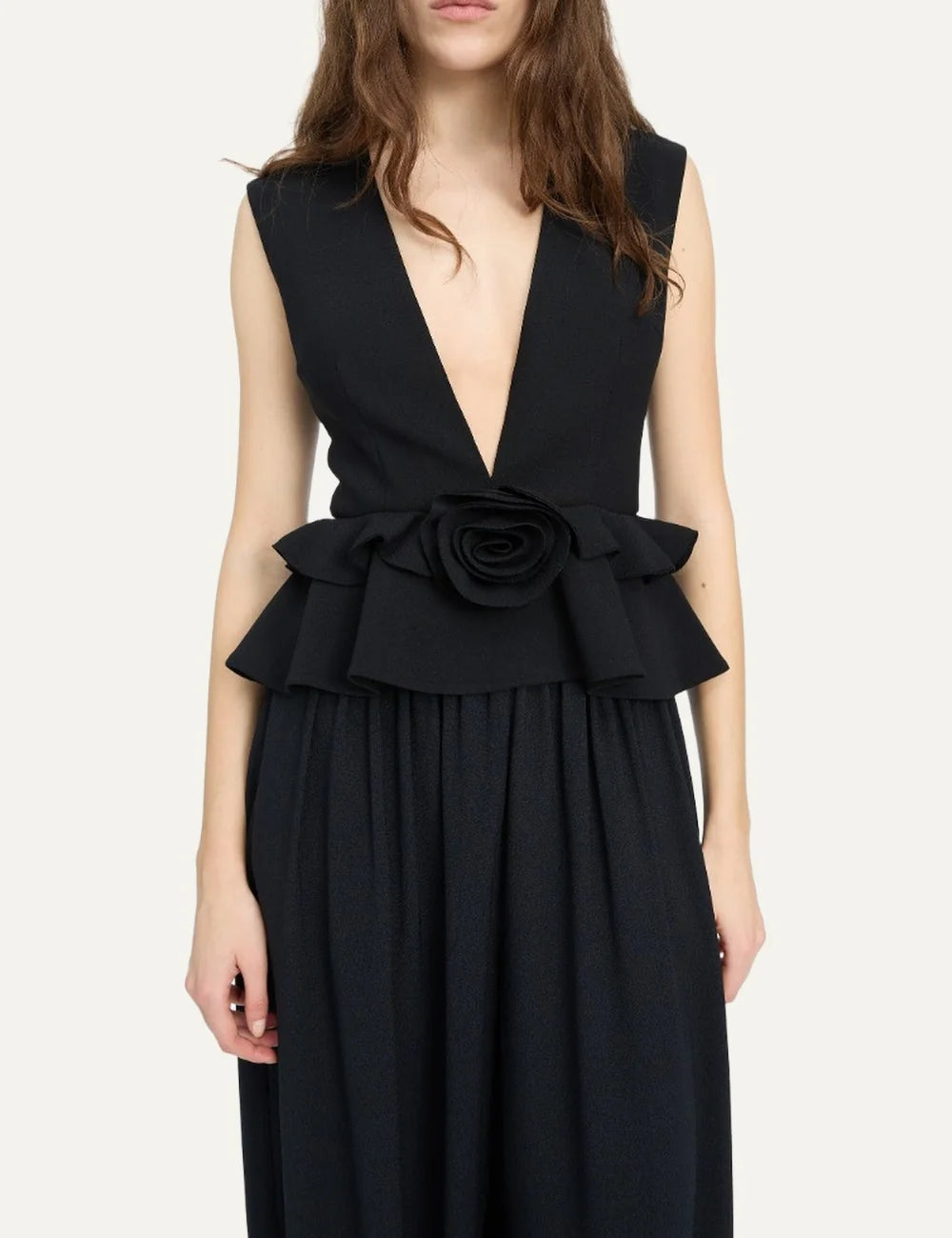 Rotate women black sleeveless V-neck top with structured shoulders, peplum hem and flower detail model