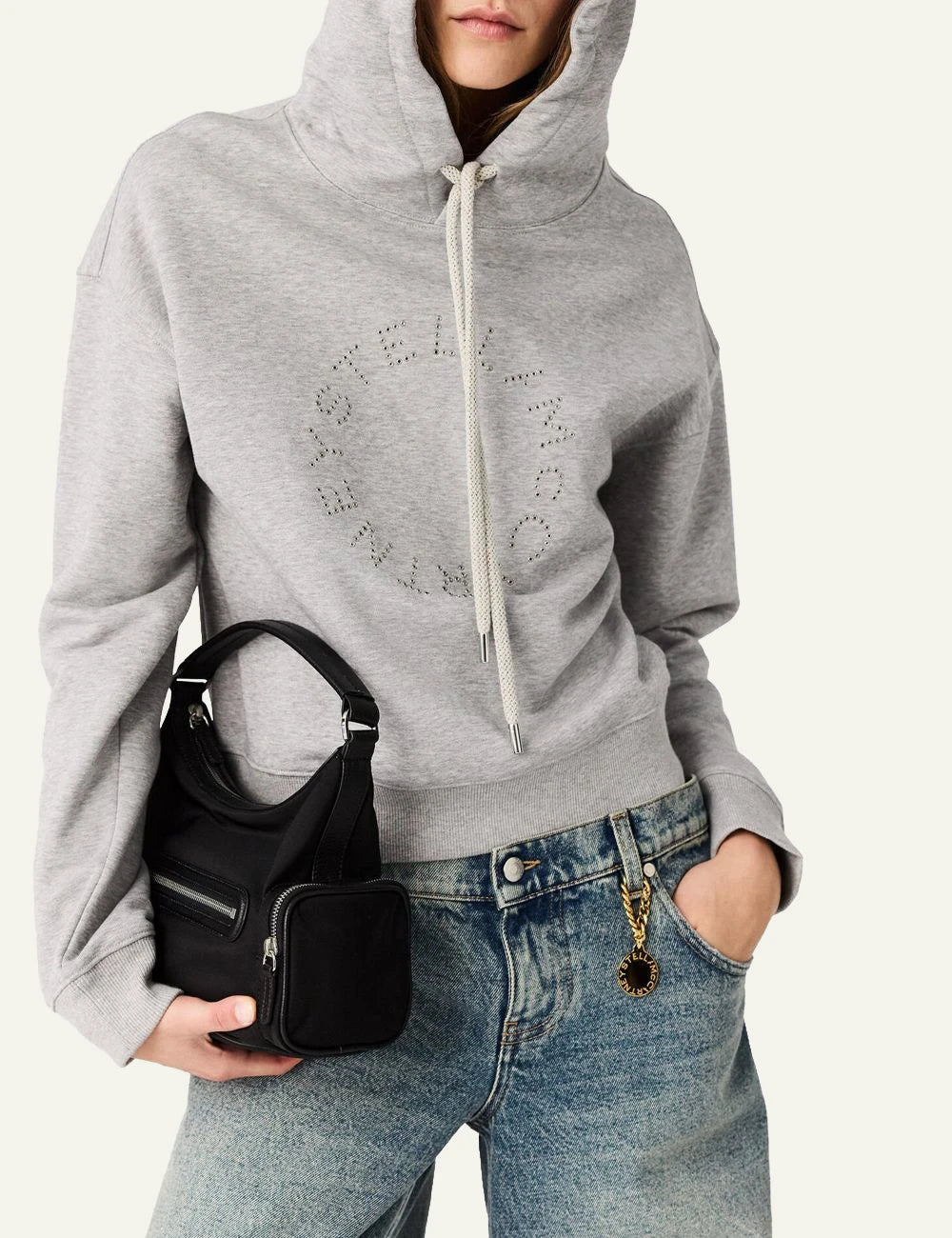 Stella McCartney shoulder bag in black vegan leather with front zip pocket, side compartments and logo coin charm, front model view