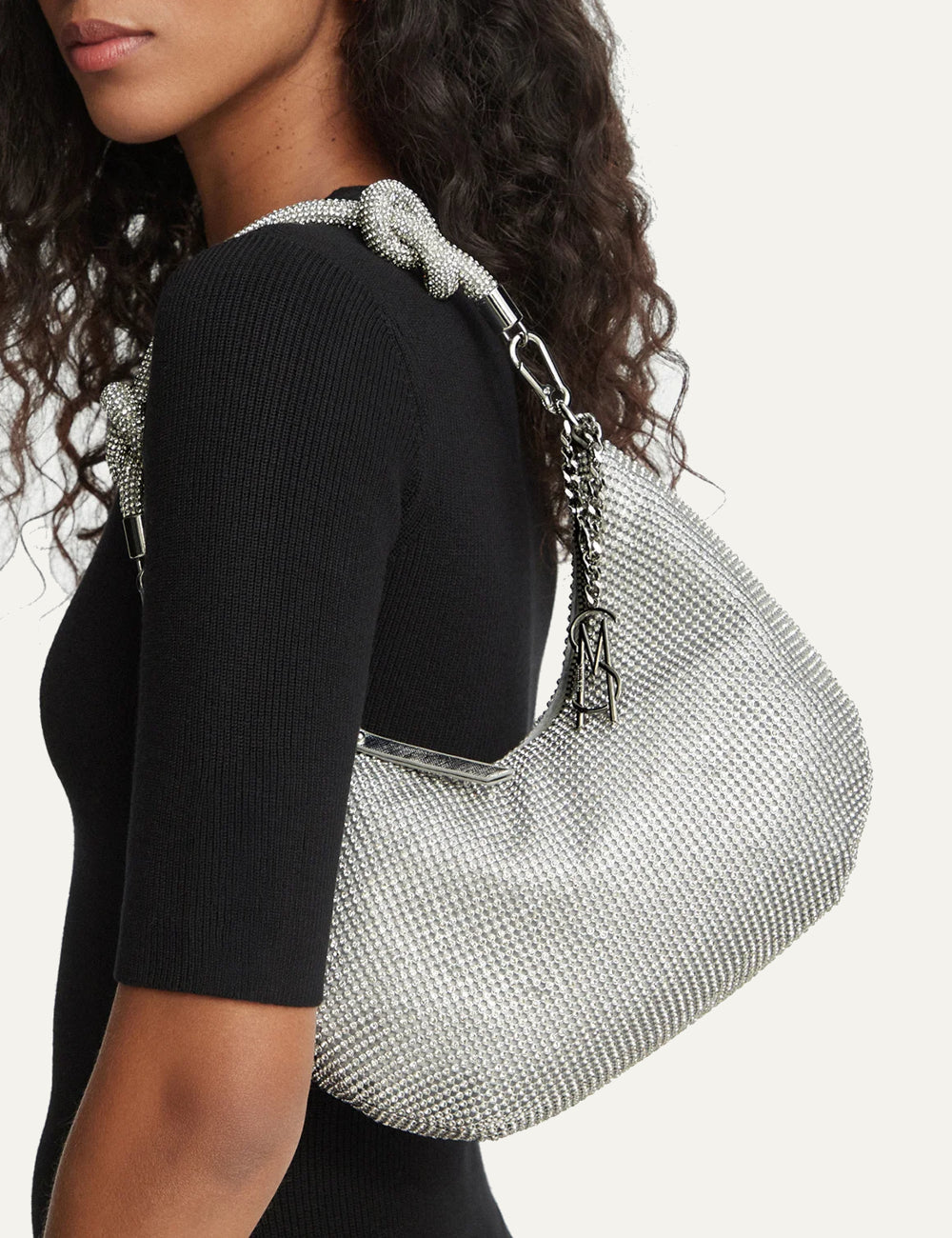 Steve Madden Bkaya women's silver rhinestone embellished shoulder bag with curved silhouette, detachable knotted rhinestone strap, silver tone hardware, side chain charm and top zipper, on model