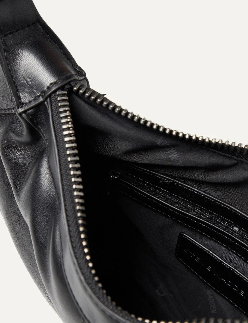 Steve Madden women's black faux leather shoulder bag with chevron quilted stitching, elongated curved silhouette, slim shoulder strap, gunmetal tone SM logo, side chain charm and top zipper, interior view